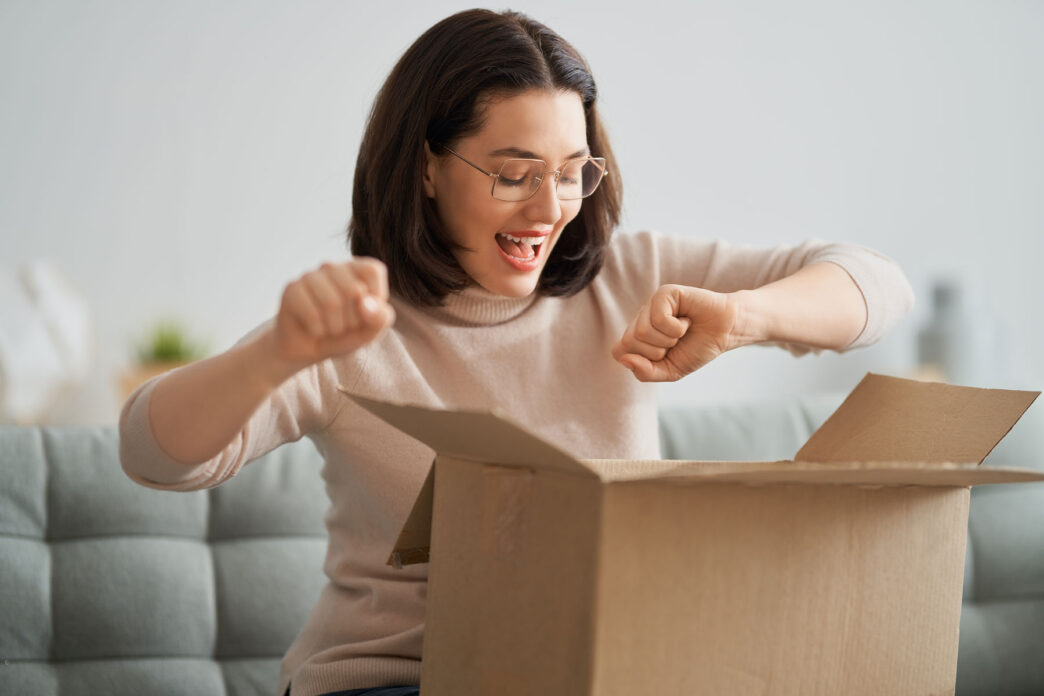 Chica joven en su casa abriendo con emoción una caja a la que está suscrita