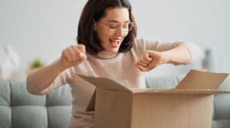 Chica joven en su casa abriendo con emoción una caja a la que está suscrita