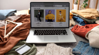 Web de moda abierta en un portátil que está en una cama llena de ropa