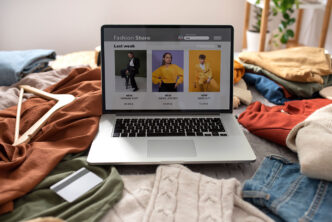 Web de moda abierta en un portátil que está en una cama llena de ropa